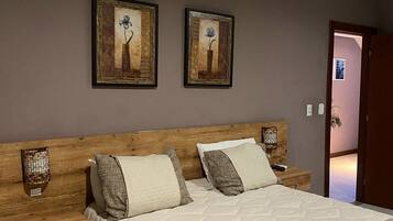 A bedroom with a wooden headboard, a large bed with a quilted cover, two bedside tables, and two framed pictures on the wall.
