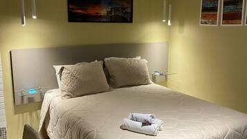Un dormitorio ordenado con una cama grande, una mesita de noche, una silla y obras de arte en las paredes.