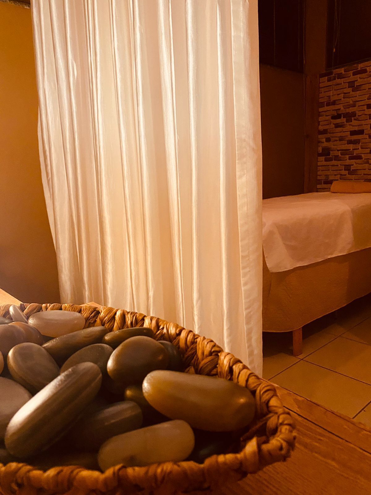 Una habitación con una cama cubierta por una sábana blanca, una cesta de piedras lisas y una cortina.
