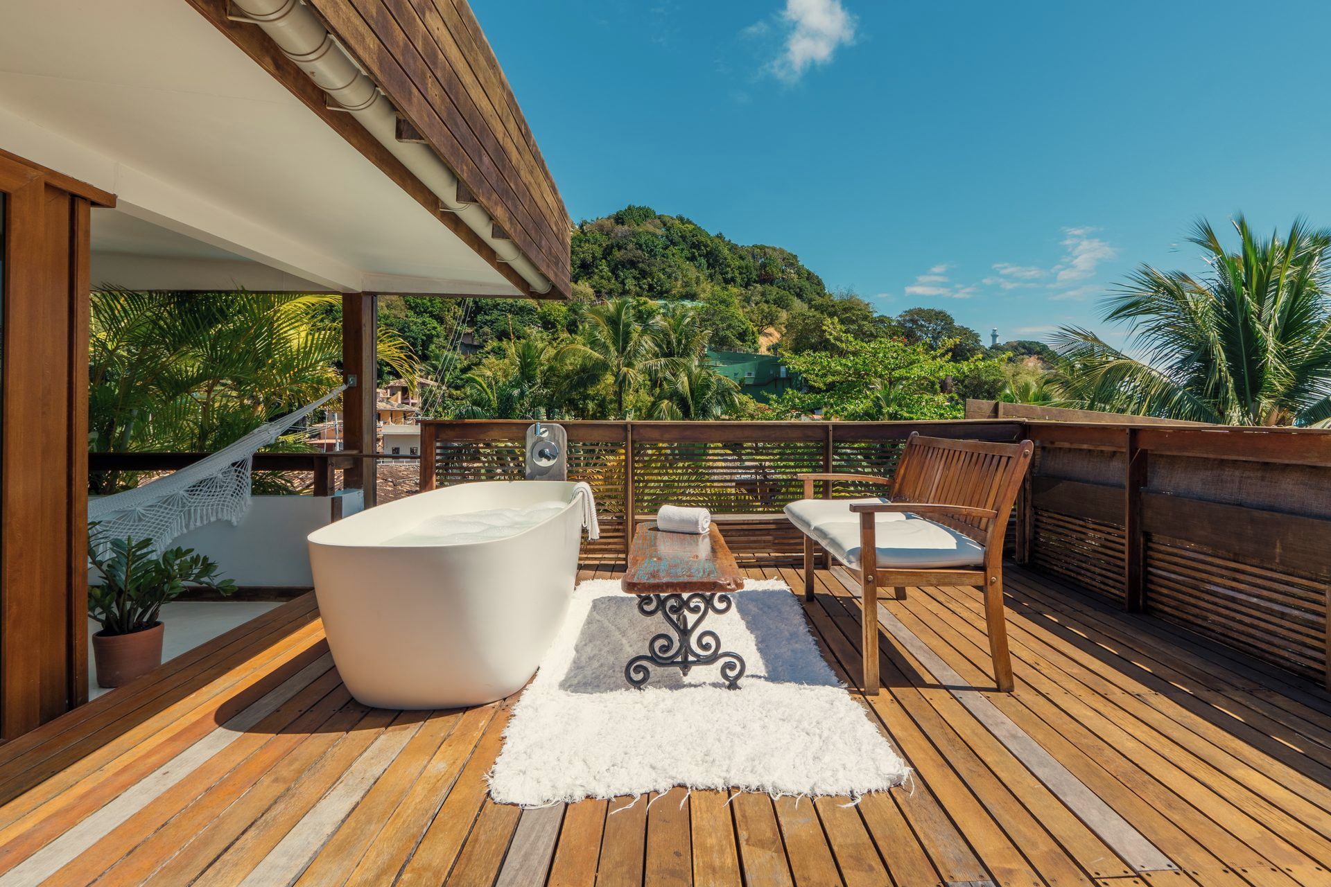 Een houten terras met een jacuzzi, twee houten stoelen en een witte vloerkleden.