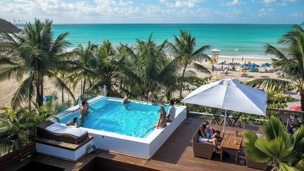 A pool area with a view of the beach and ocean, surrounded by palm trees. - Pousada Sambass (Cairu)