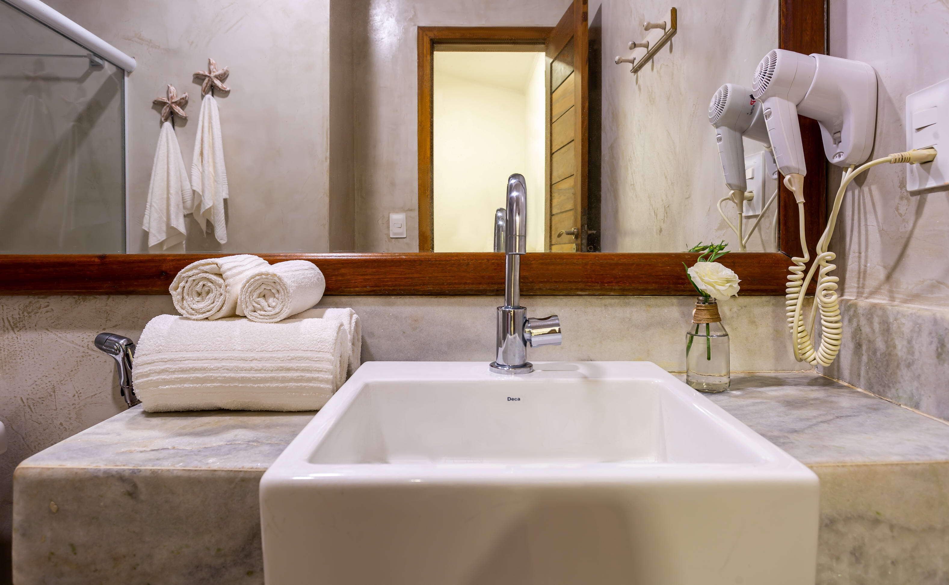 Une salle de bain avec un lavabo blanc, un miroir et un sèche-cheveux fixé au mur.