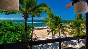 A beach view from a covered area with palm trees and umbrellas. - Pousada Sambass (Cairu)
