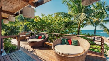 Une terrasse en bois, meublée de mobilier en osier, avec vue sur l’océan.