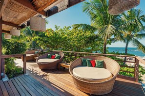 A wooden deck with wicker furniture and a view of the ocean. - Pousada Sambass (Cairu)