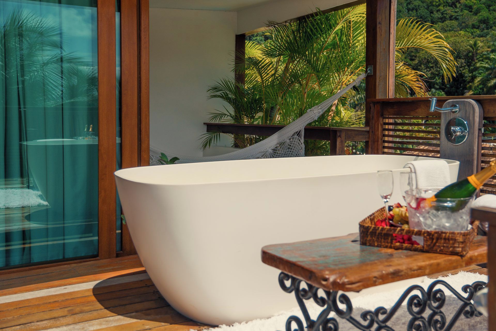A modern bathroom with a freestanding bathtub, a glass shower enclosure, and a wooden table with a bottle and fruit basket.