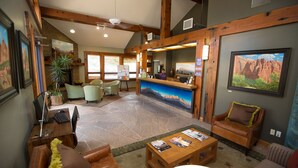 A lobby with a reception desk, seating area, and a large painting of a mountain landscape. - Desert Pearl Inn (Springdale)