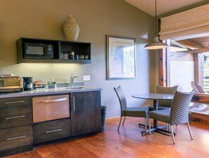 A modern kitchen with a microwave, toaster, and coffee maker, a dining area with wicker chairs, and a framed artwork on the wall.