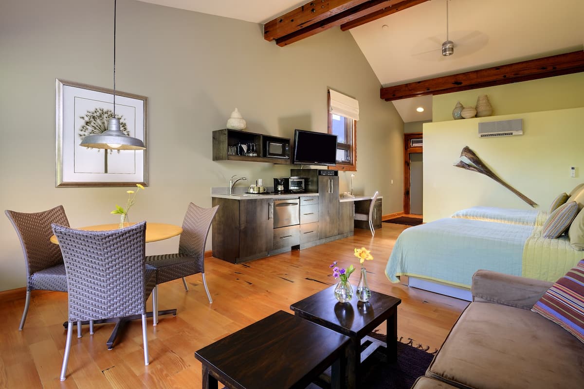 A modern, well-lit room with a dining area, kitchenette, and a large bed.