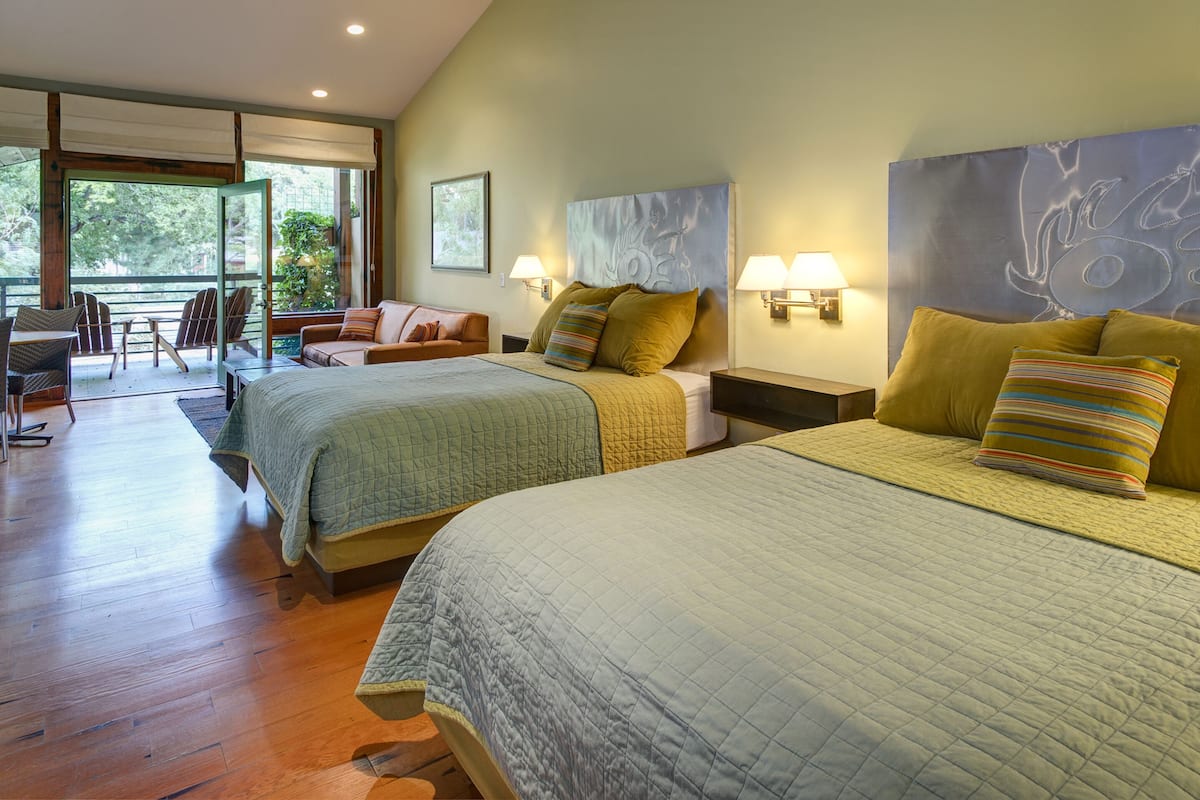 A hotel room with two beds, a balcony, a desk, and a chair.