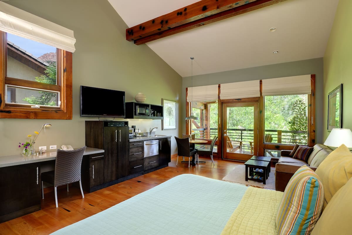 A spacious room with a large bed, a dining area, a kitchen, and a balcony with a view of the outdoors.