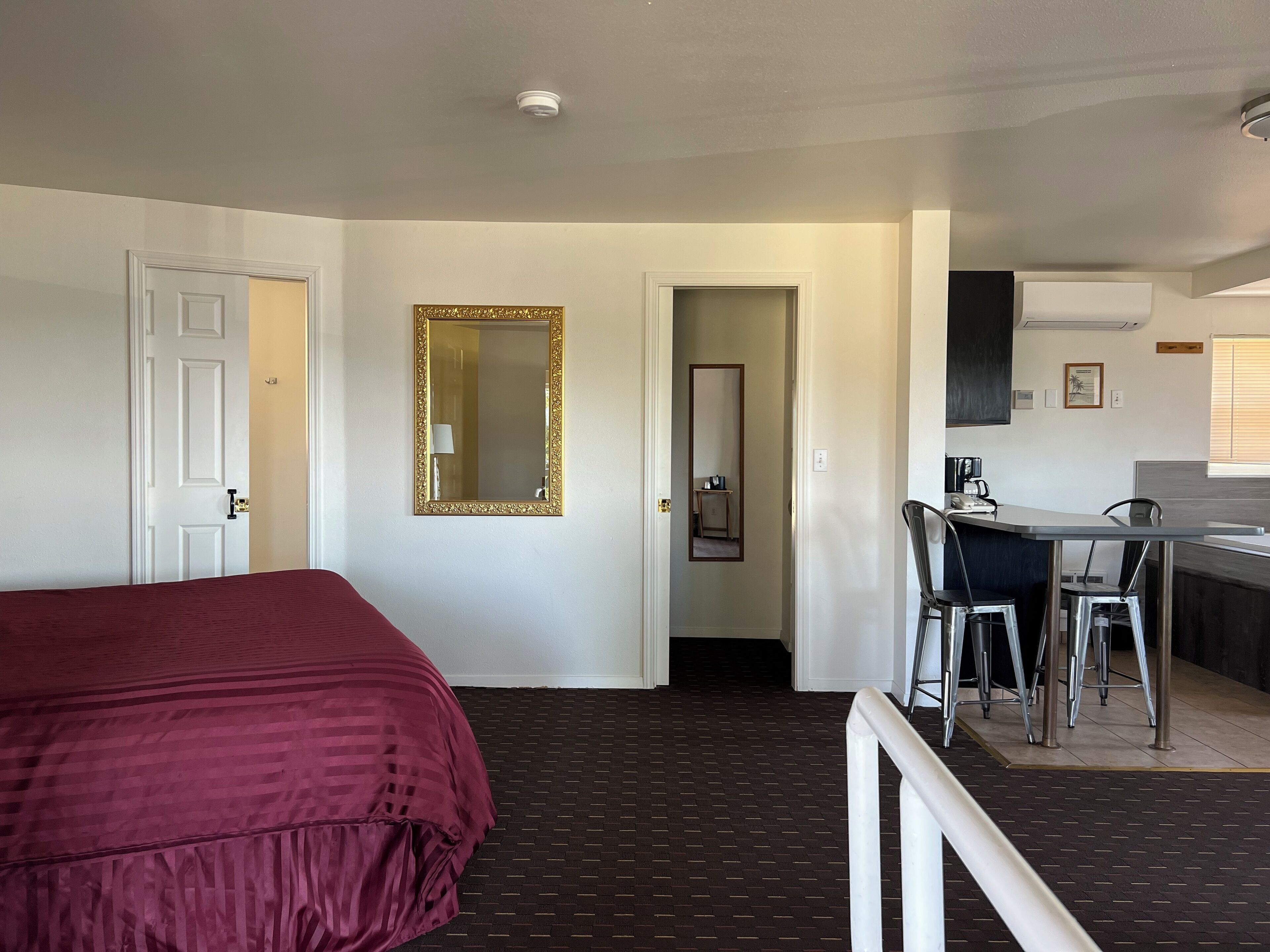 A hotel room with a bed, a desk with chairs, a mirror, and a kitchenette.