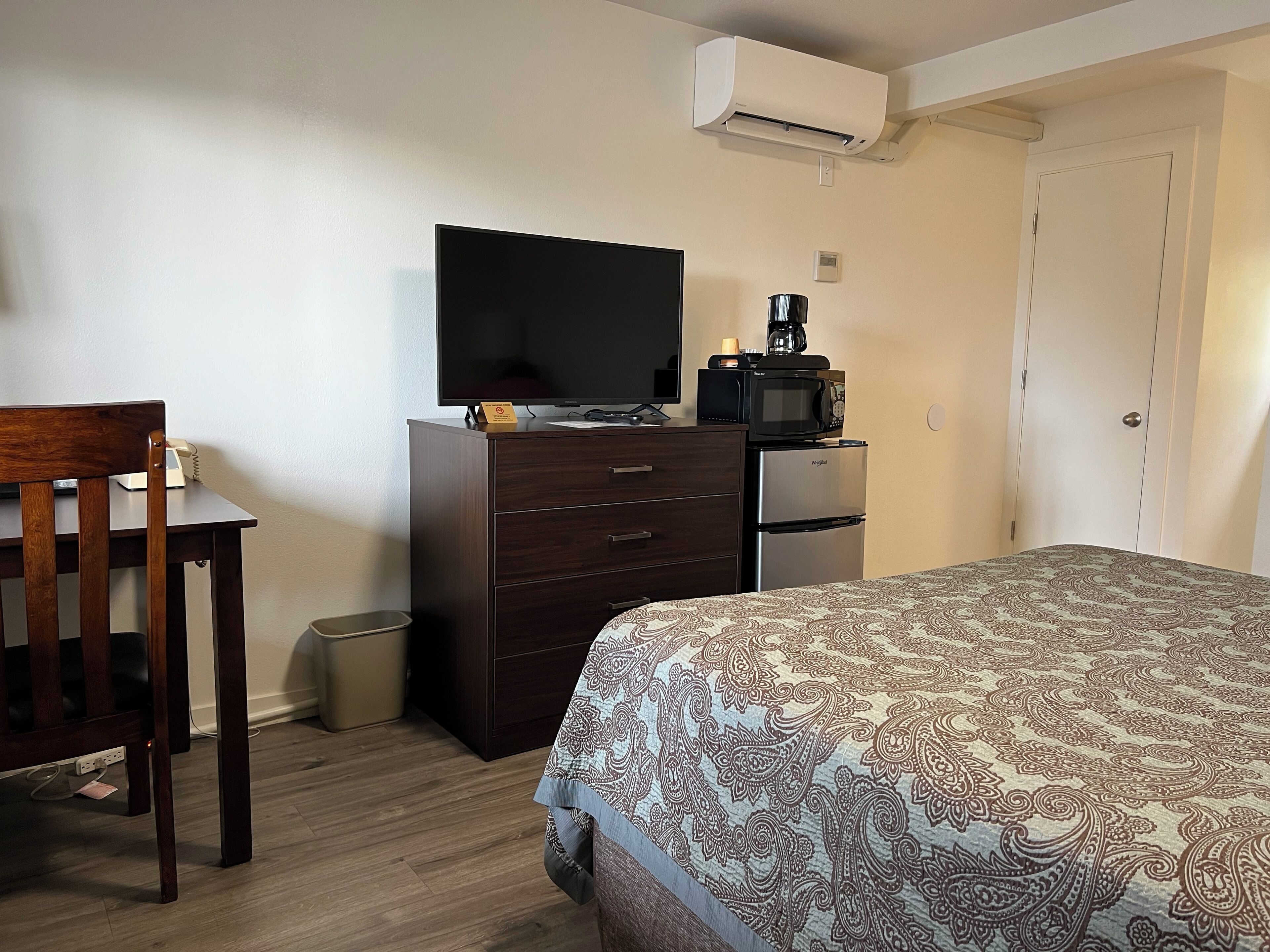 Una habitación de hotel con cama, escritorio con televisor, microondas y refrigerador.