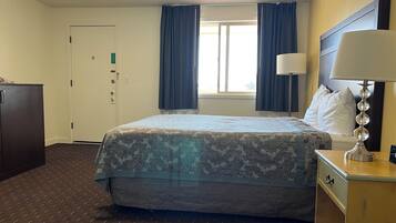 A hotel room with a bed, a desk, a lamp, a wardrobe, and a window with curtains.