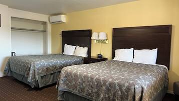 A hotel room with two beds, a nightstand with a lamp, a clock, and a wall-mounted air conditioner.