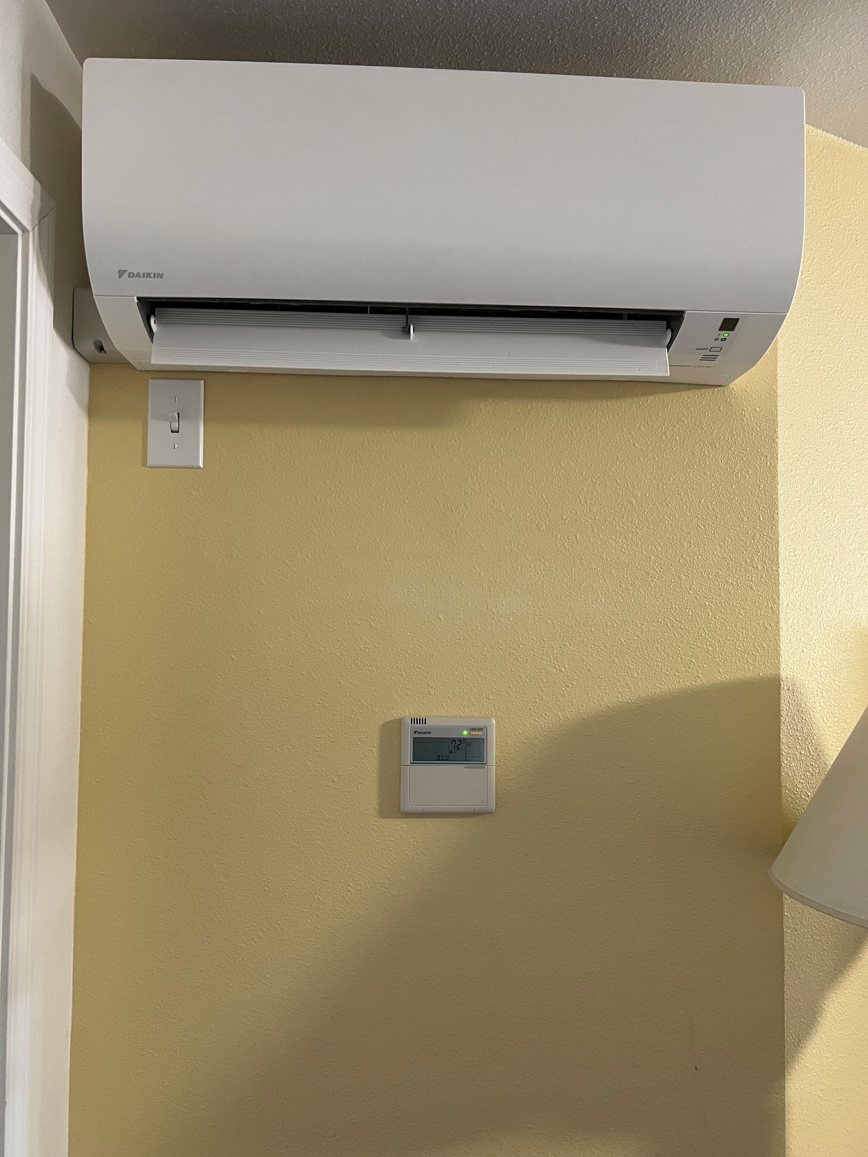 An air conditioning unit mounted on a wall with a thermostat below it.