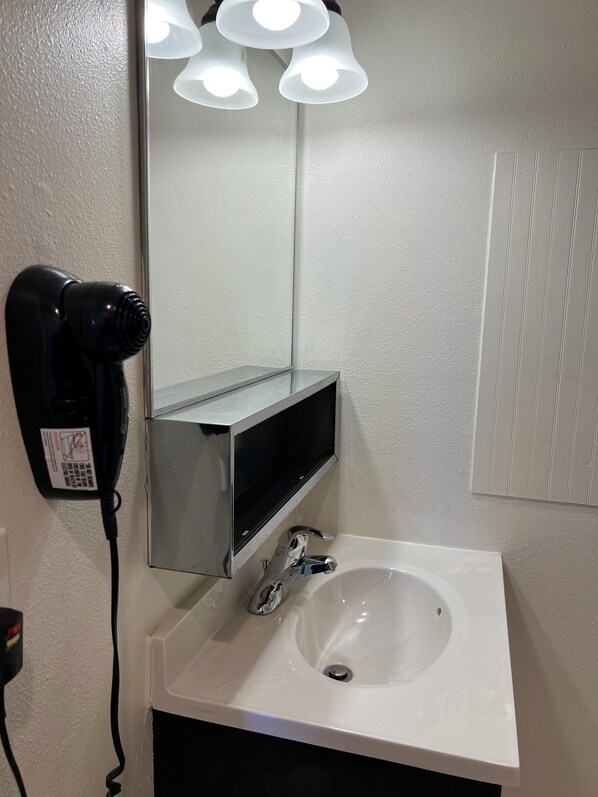 A bathroom with a white sink, a mirror, and a hairdryer on the wall. - Port Townsend Inn (Port Townsend)