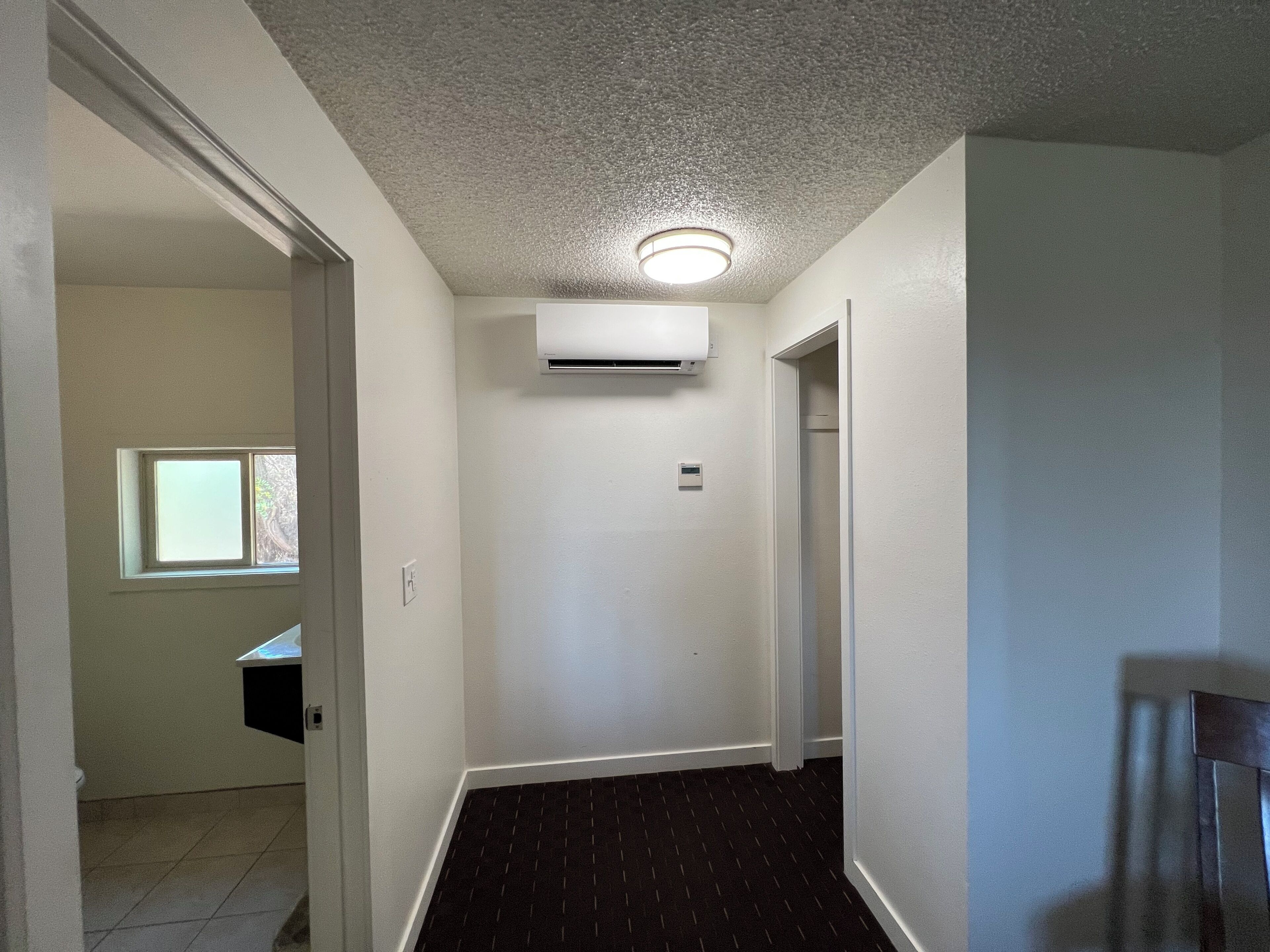 Een smalle gang met een betegelde vloer, een airconditioner aan de muur en een deur naar een andere kamer.