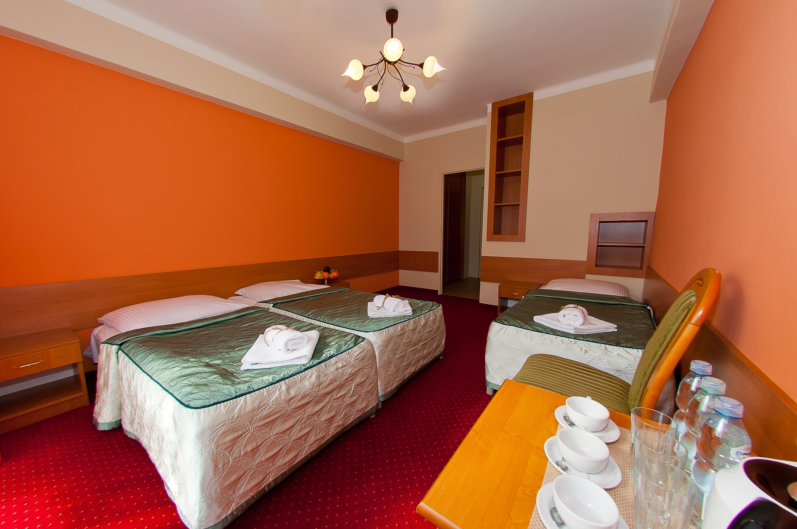 Quarto de hotel com duas camas, uma mesa de cabeceira de madeira, uma mesa com tigelas e copos, e um espelho.