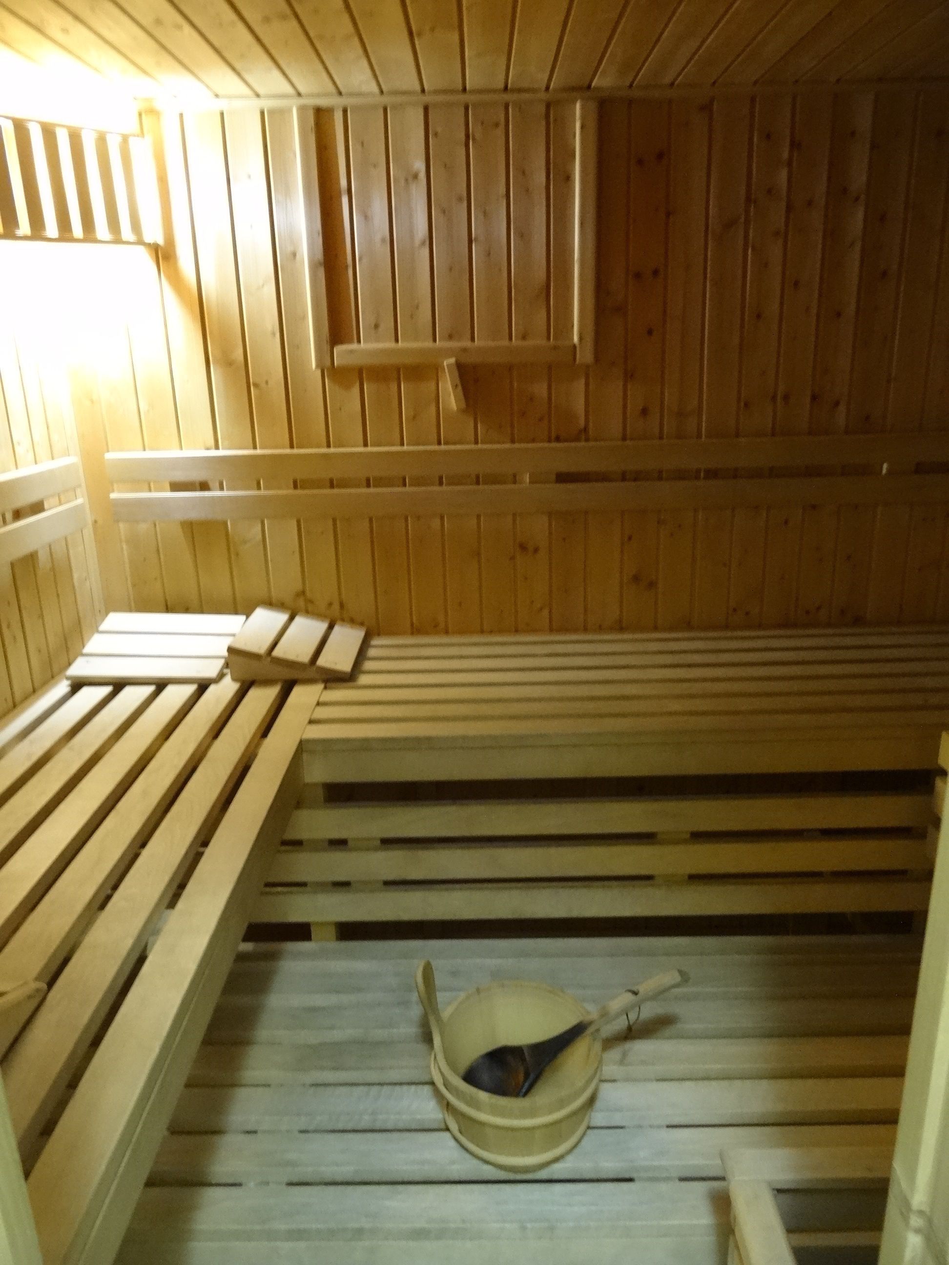 A sauna room with wooden benches and a wooden bucket with a spoon.