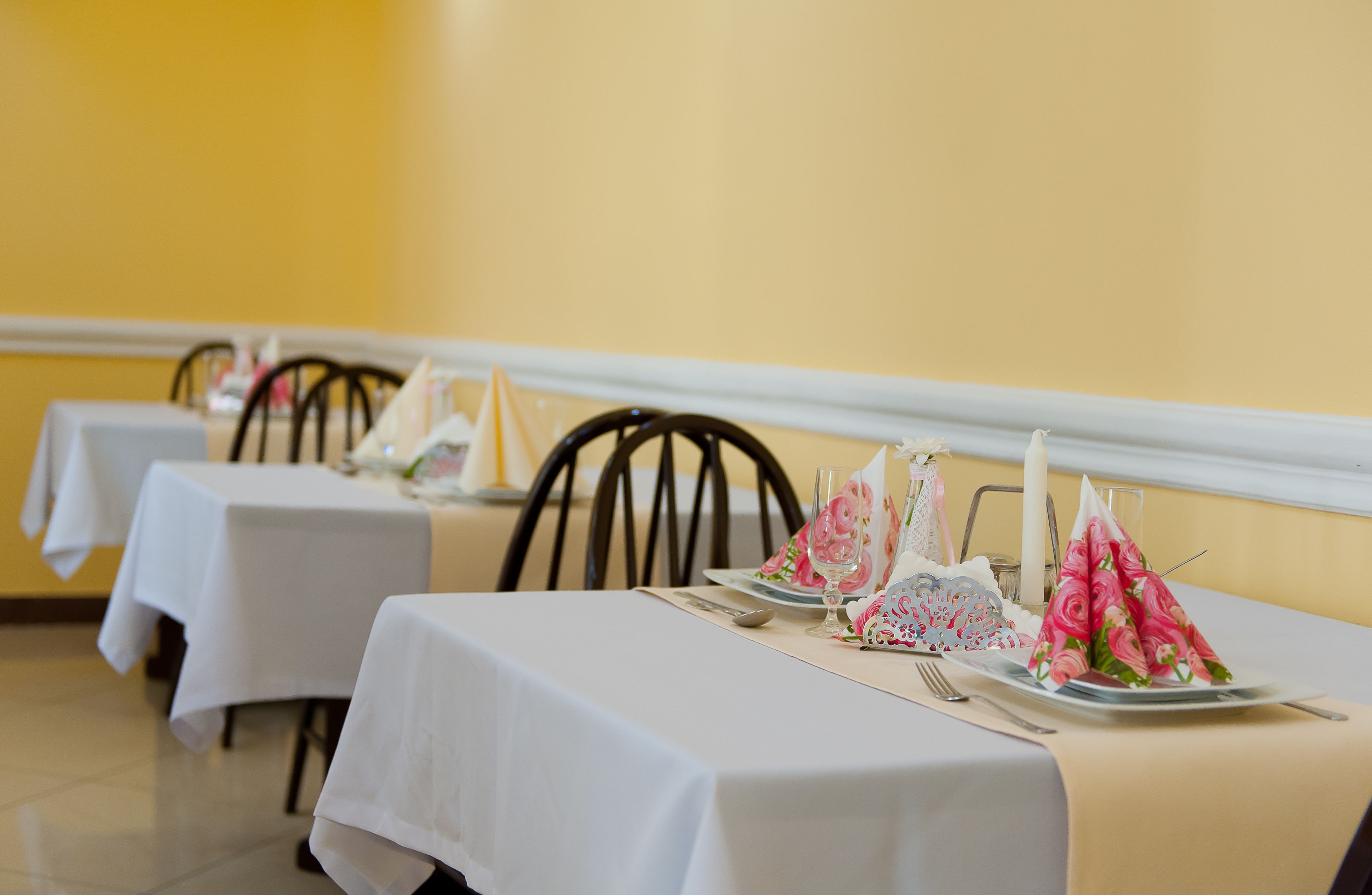 Een eetgedeelte met gedekte tafels, voorzien van witte tafelkleden en decoratieve servetten met bloemen.