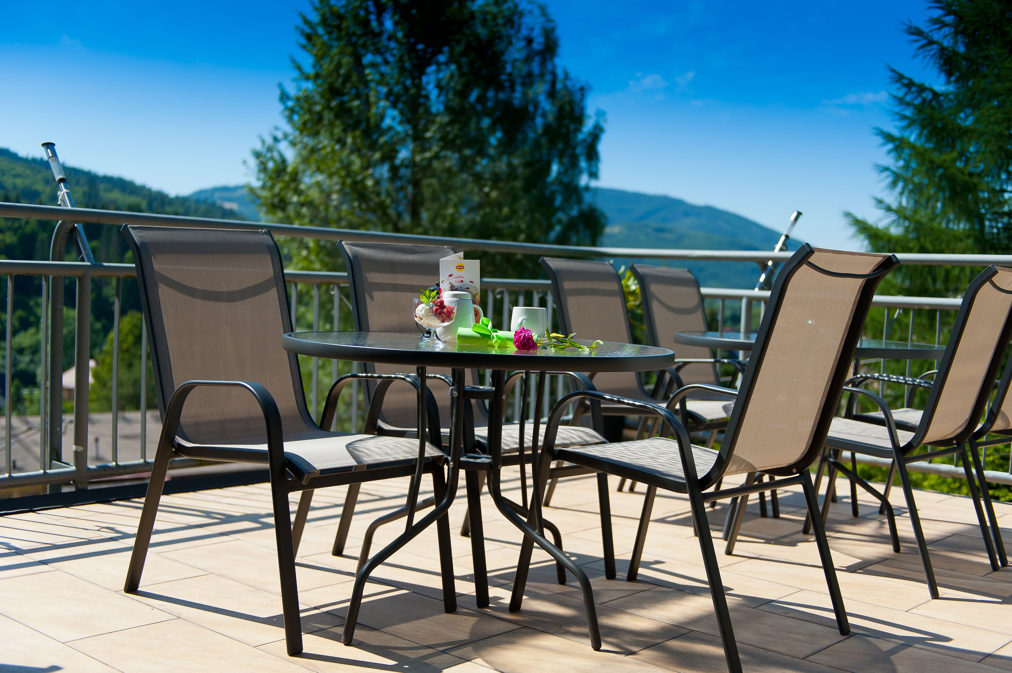 Une table ronde entourée de chaises, sur un balcon offrant une vue sur les montagnes et les arbres.