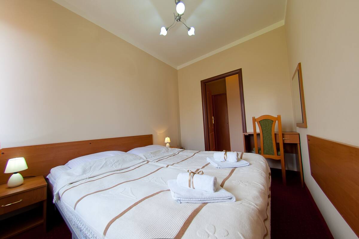 Hotellihuone, jossa on suuri sänky, kaksi yöpöytää valaisimineen, puinen sängynpääty, peili ja ovi.