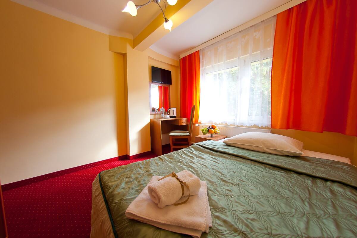 Hotellihuone, jossa on sänky, työpöytä, tuoli, televisio ja ikkuna, jossa on verhot.