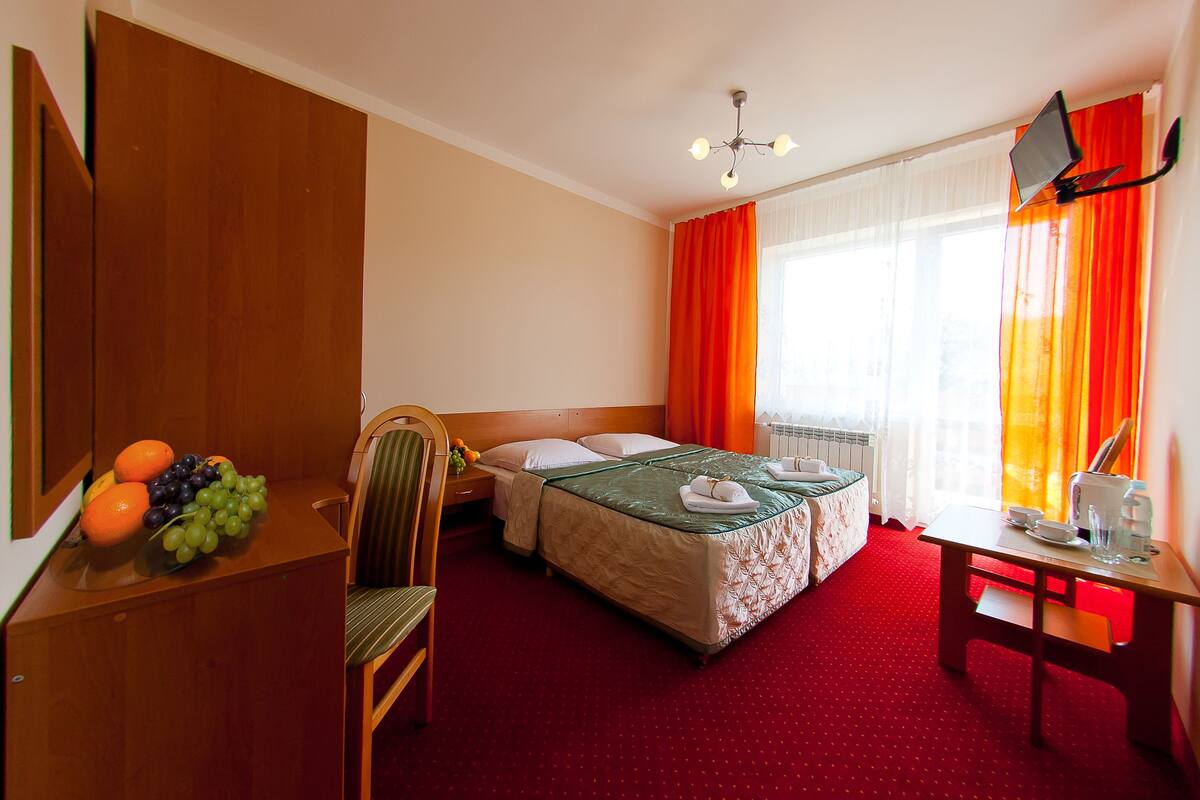 Hotellihuone, jossa on sänky, työpöytä, tuoli, televisio ja hedelmäkulho.
