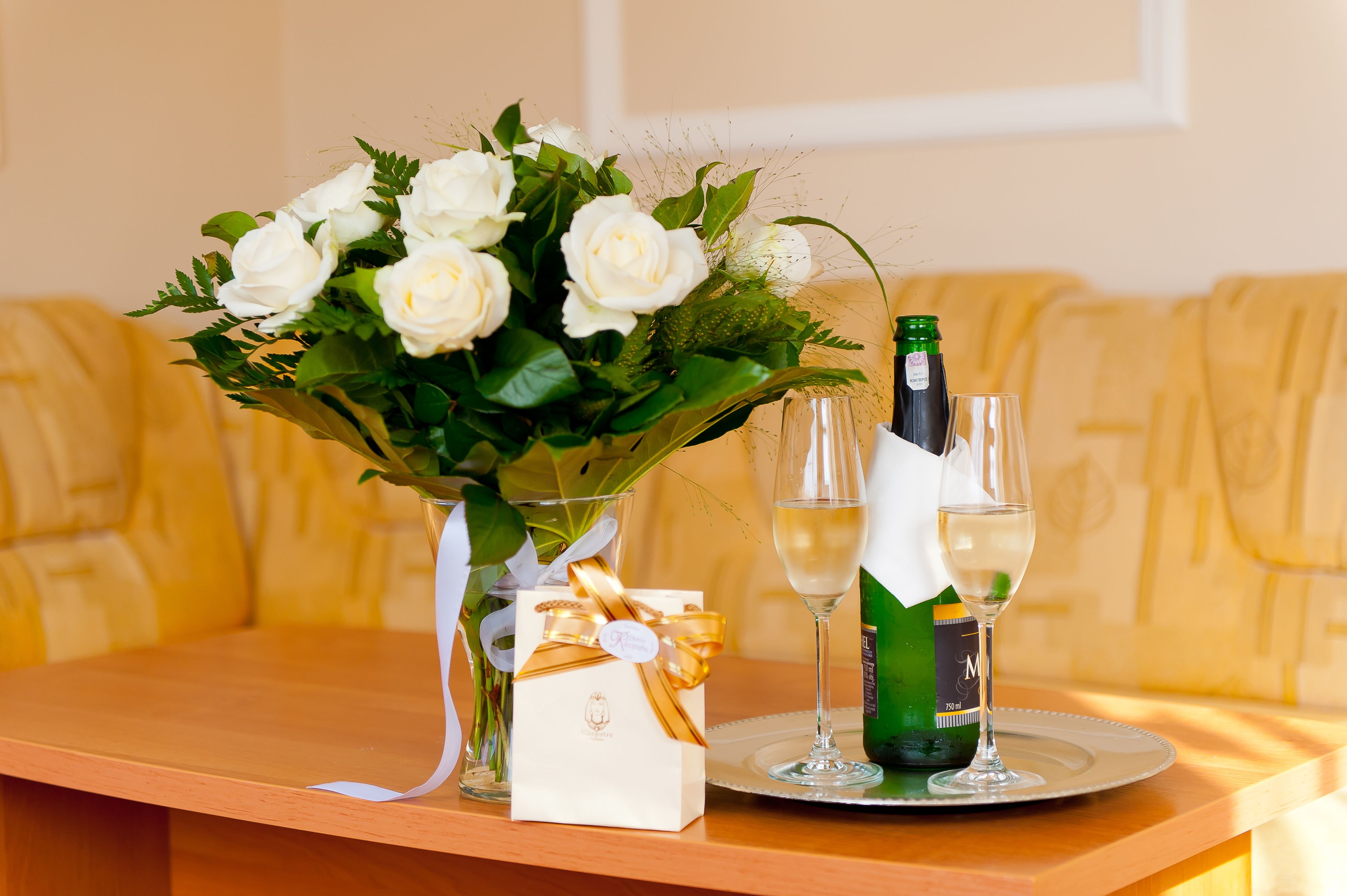 A table with a bouquet of white roses, a bottle of champagne, and a gift box.