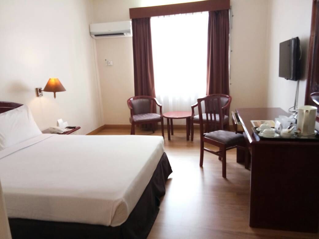 A hotel room with a bed, a desk with a chair, a small table, and a TV.