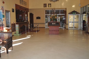 Un vestíbulo amplio con una recepción, un banco de madera, una entrada con puerta de vidrio y un centro de mesa con planta decorativa.
