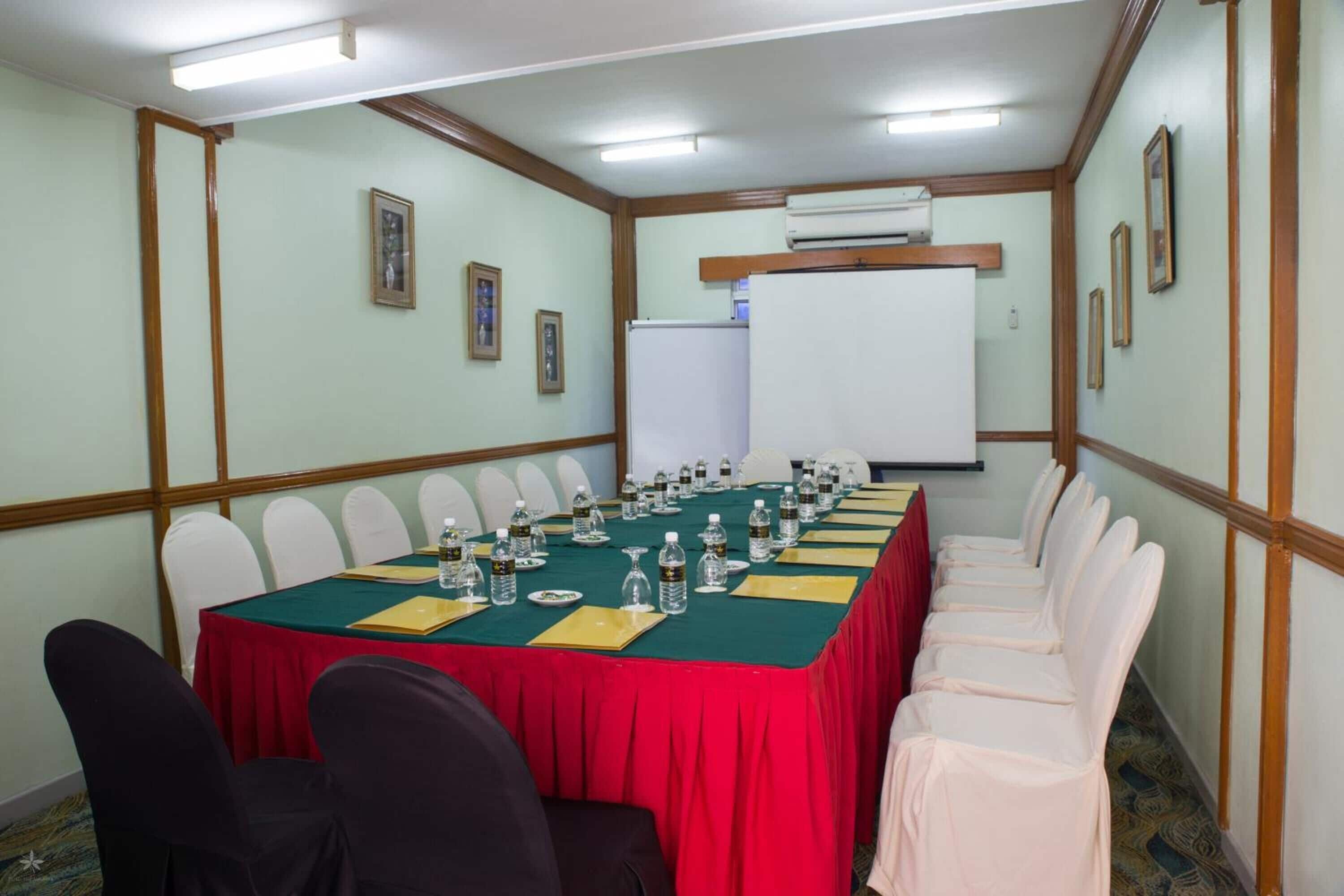 Uma sala de conferências com uma mesa comprida, cadeiras brancas e um quadro branco.