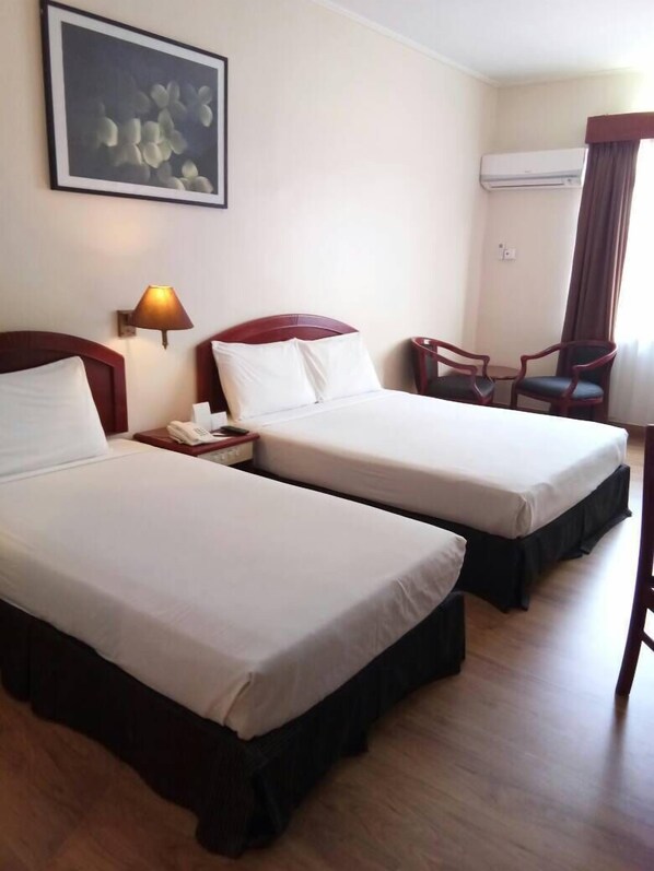 Habitación de hotel con dos camas, una lámpara de noche, una silla, un equipo de aire acondicionado y un cuadro en la pared.