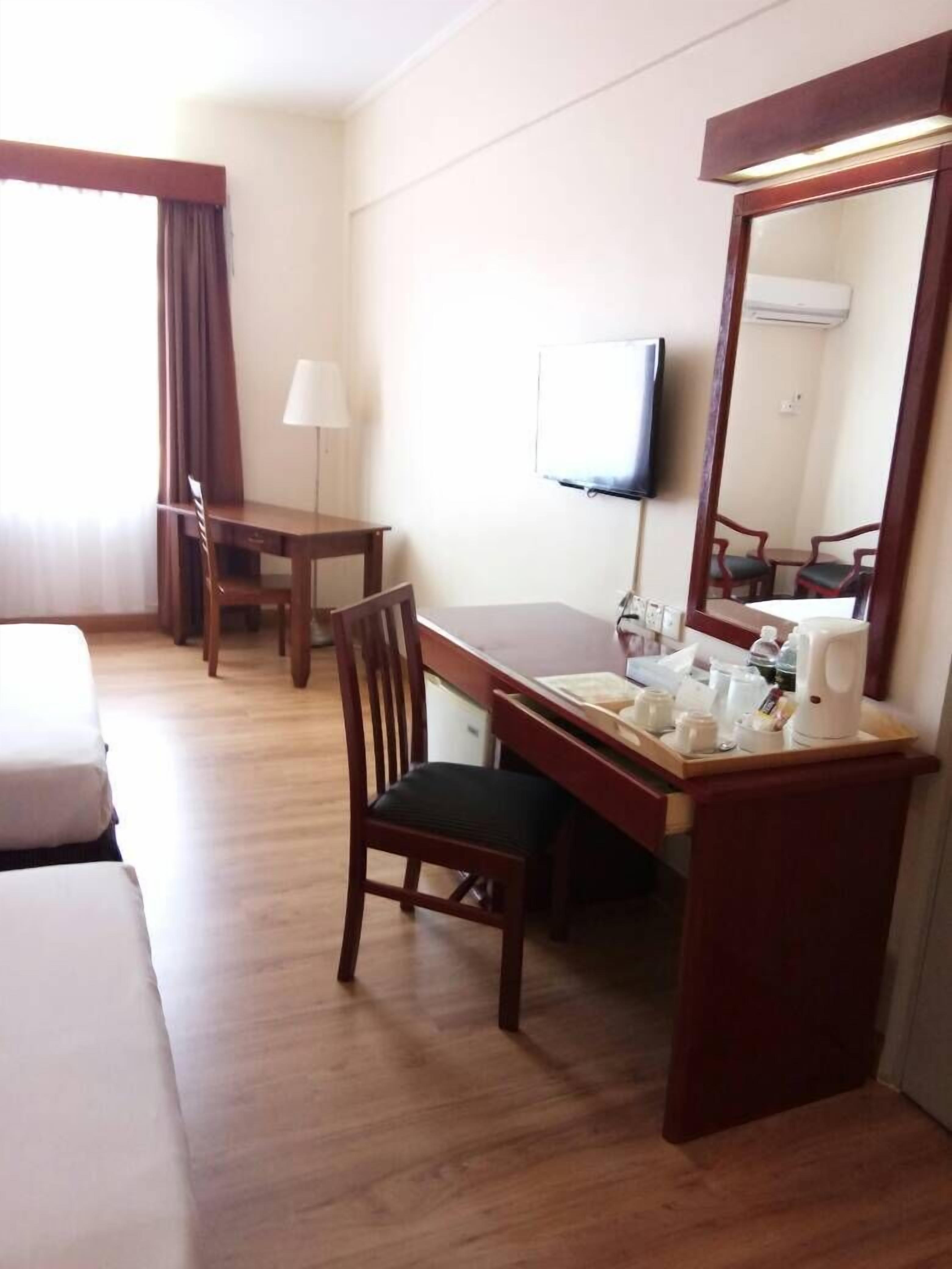 A hotel room with a wooden desk, a chair, a bed, a TV, and a mirror.