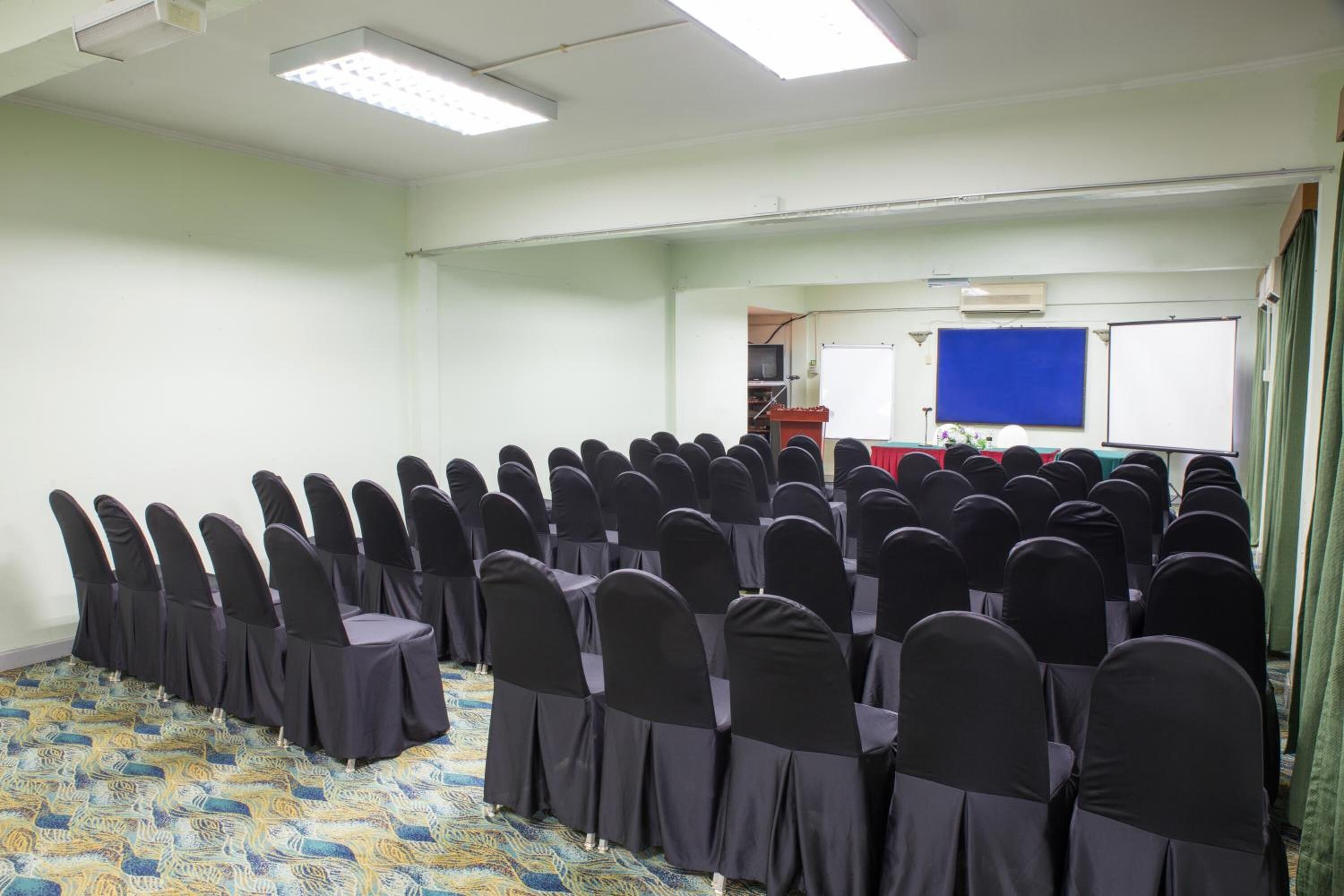 A conference room with rows of chairs covered in black fabric, a carpeted floor, and a whiteboard in the background.