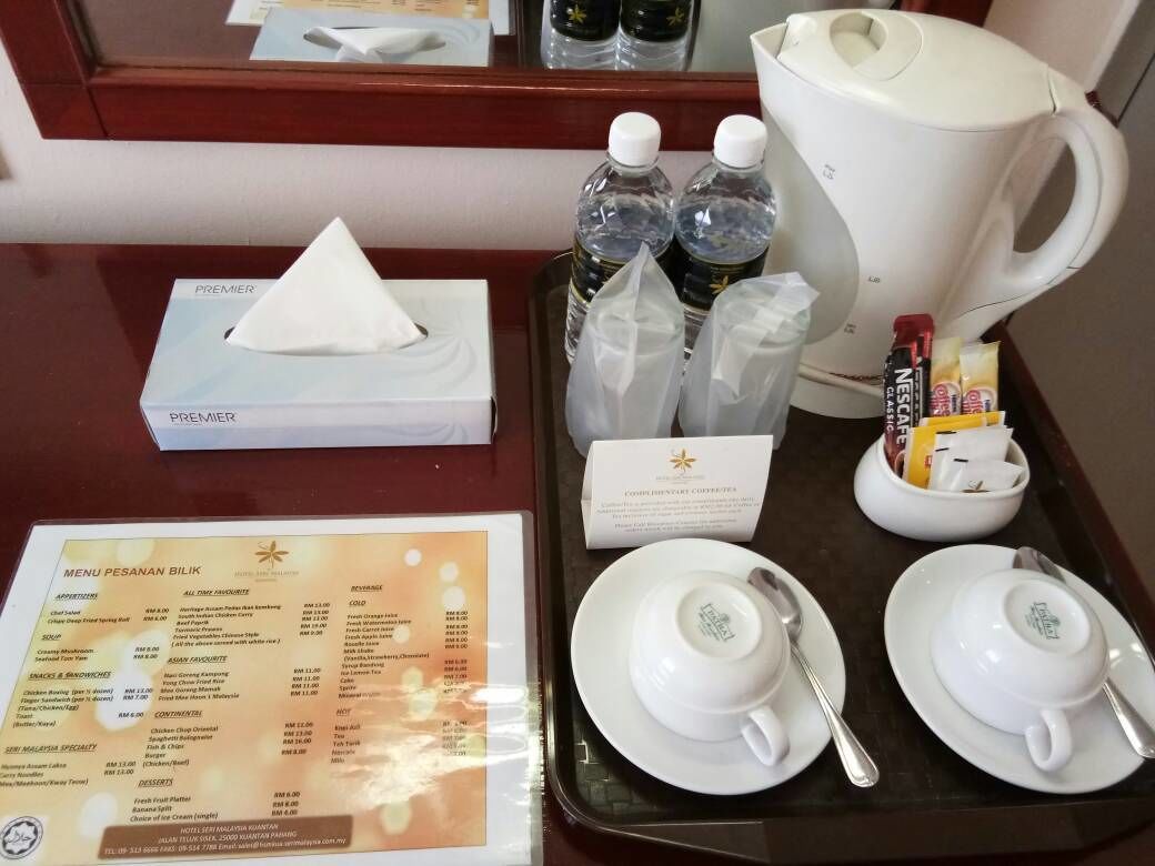 A hotel room's breakfast tray with a menu, a coffee pot, bottled water, and a small dish of orange juice.