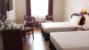 A hotel room with two beds, a desk with a chair, a TV, and an air conditioning unit.