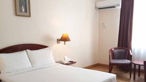 A hotel room with a large bed, a bedside table with a lamp, a chair, an air conditioning unit, and a framed picture on the wall. - Hotel Seri Malaysia Kuantan (Kuantan)