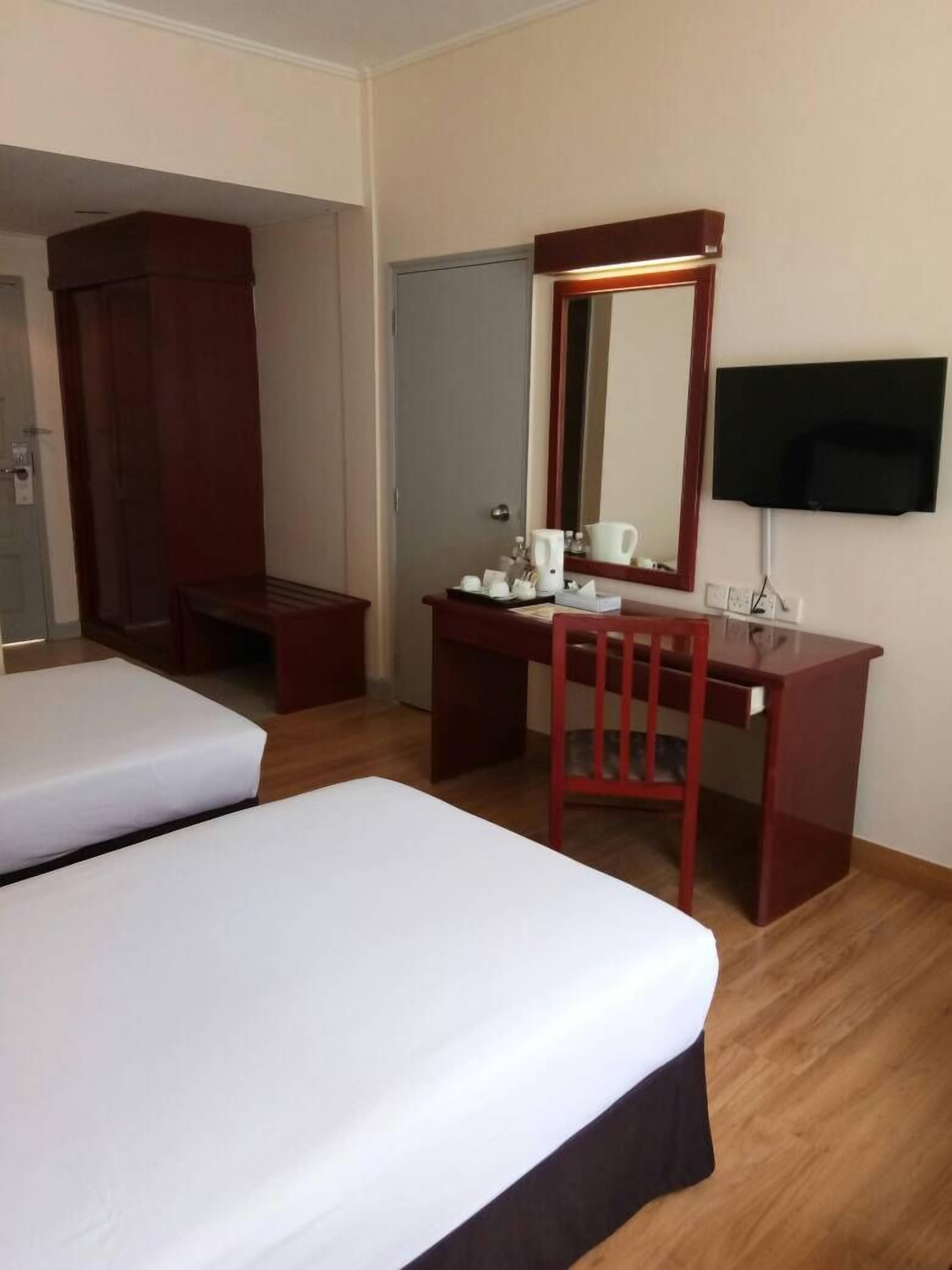 A hotel room with two single beds, a wooden desk with a chair, a mirror, a television mounted on the wall, and a door leading to another room.