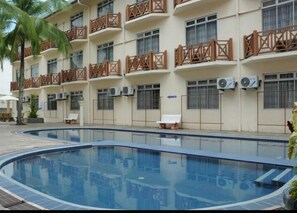 Un hotel con piscina, varios balcones con barandillas de madera y unidades de aire acondicionado en las paredes exteriores.