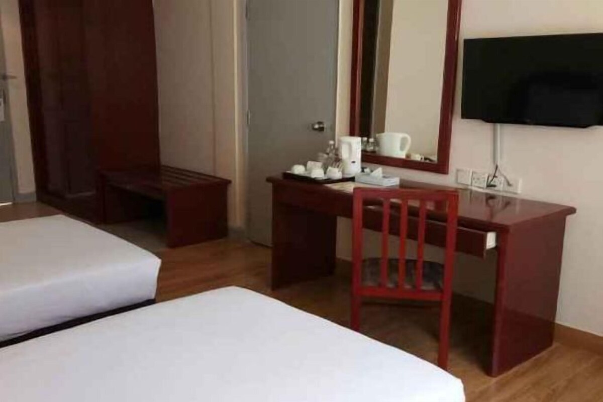 A hotel room with two beds, a desk, a chair, a television, and a small table with a cup and saucer.
