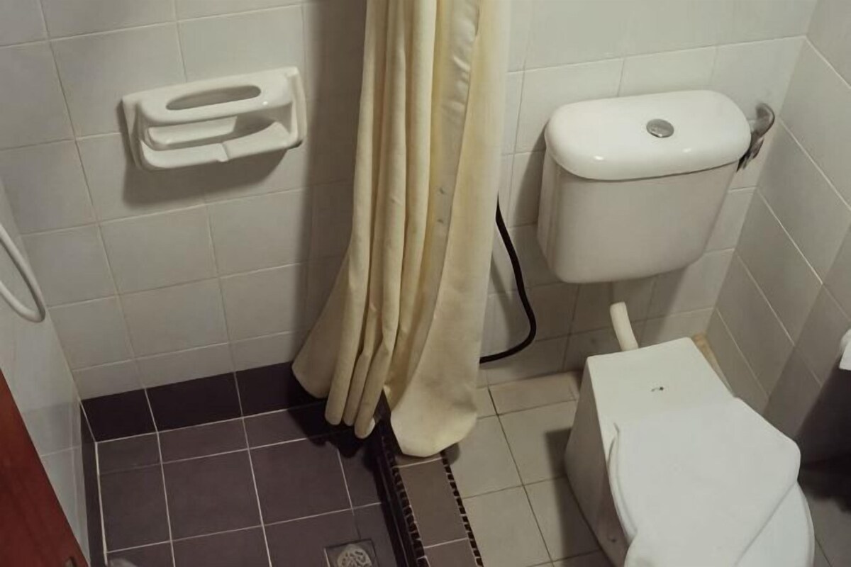 A bathroom with a toilet, a shower curtain, and a hand dryer.