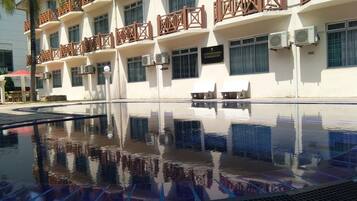 A hotel with a swimming pool, multiple balconies, and air conditioning units.