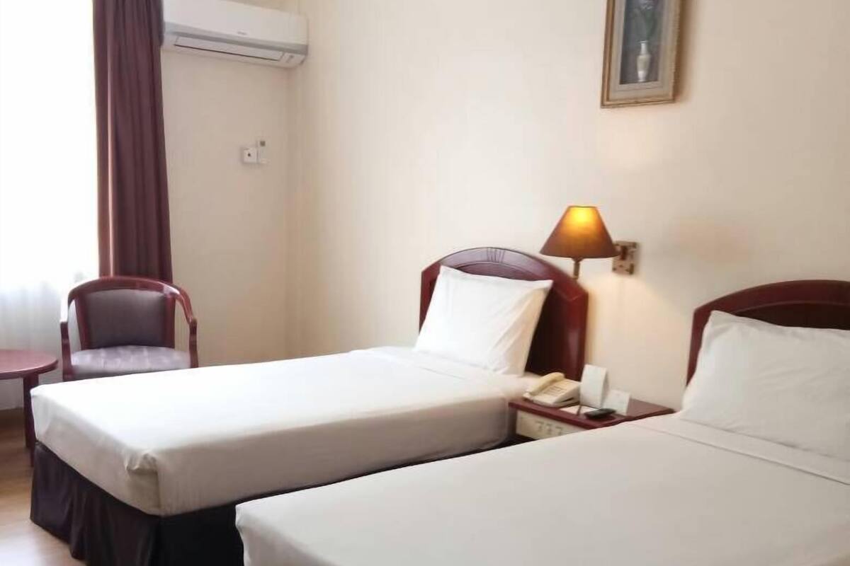 A hotel room with two single beds, a chair, a desk, and a lamp.