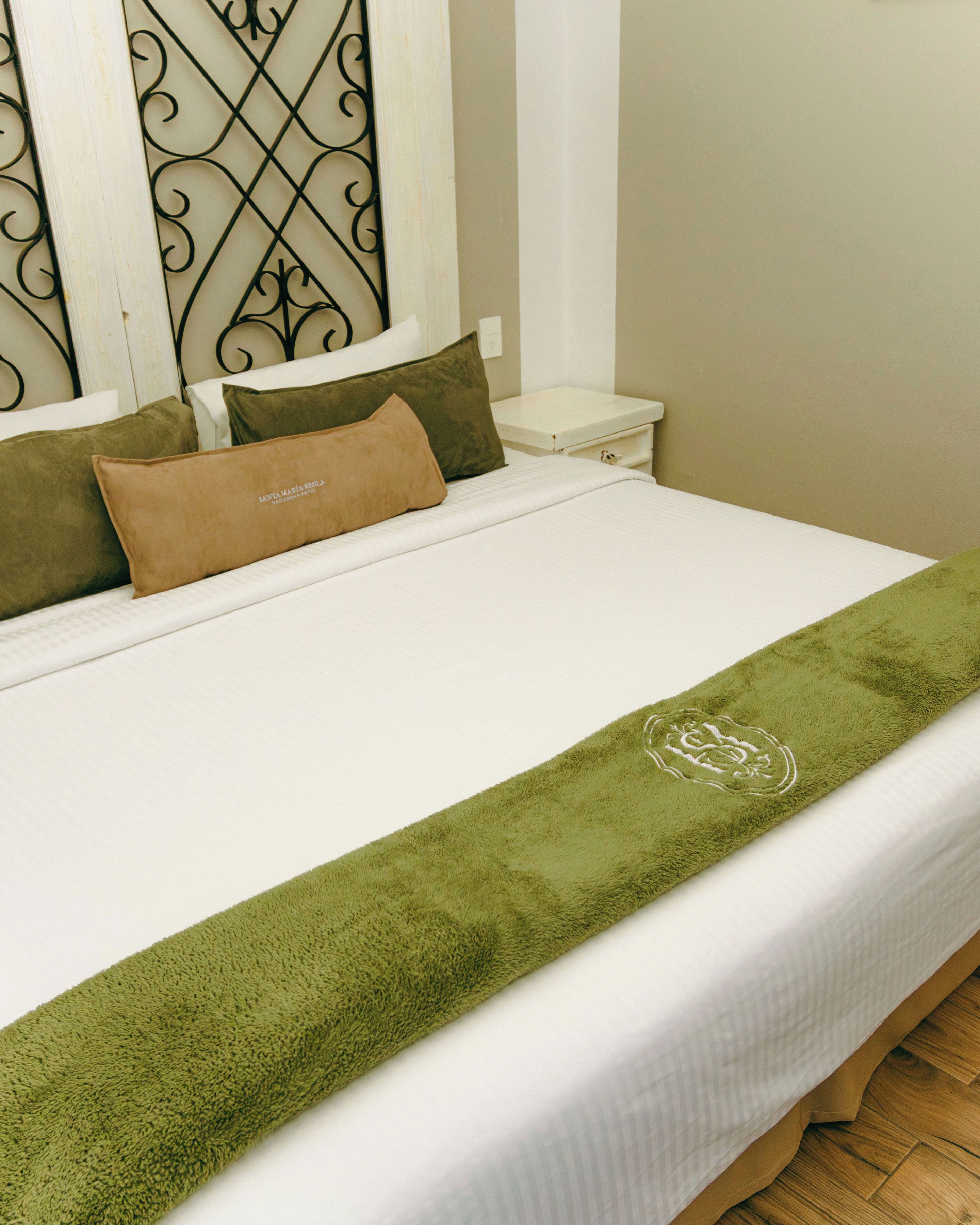 Una cama bien tendida con una toalla verde, dos almohadas y un cabecero blanco.