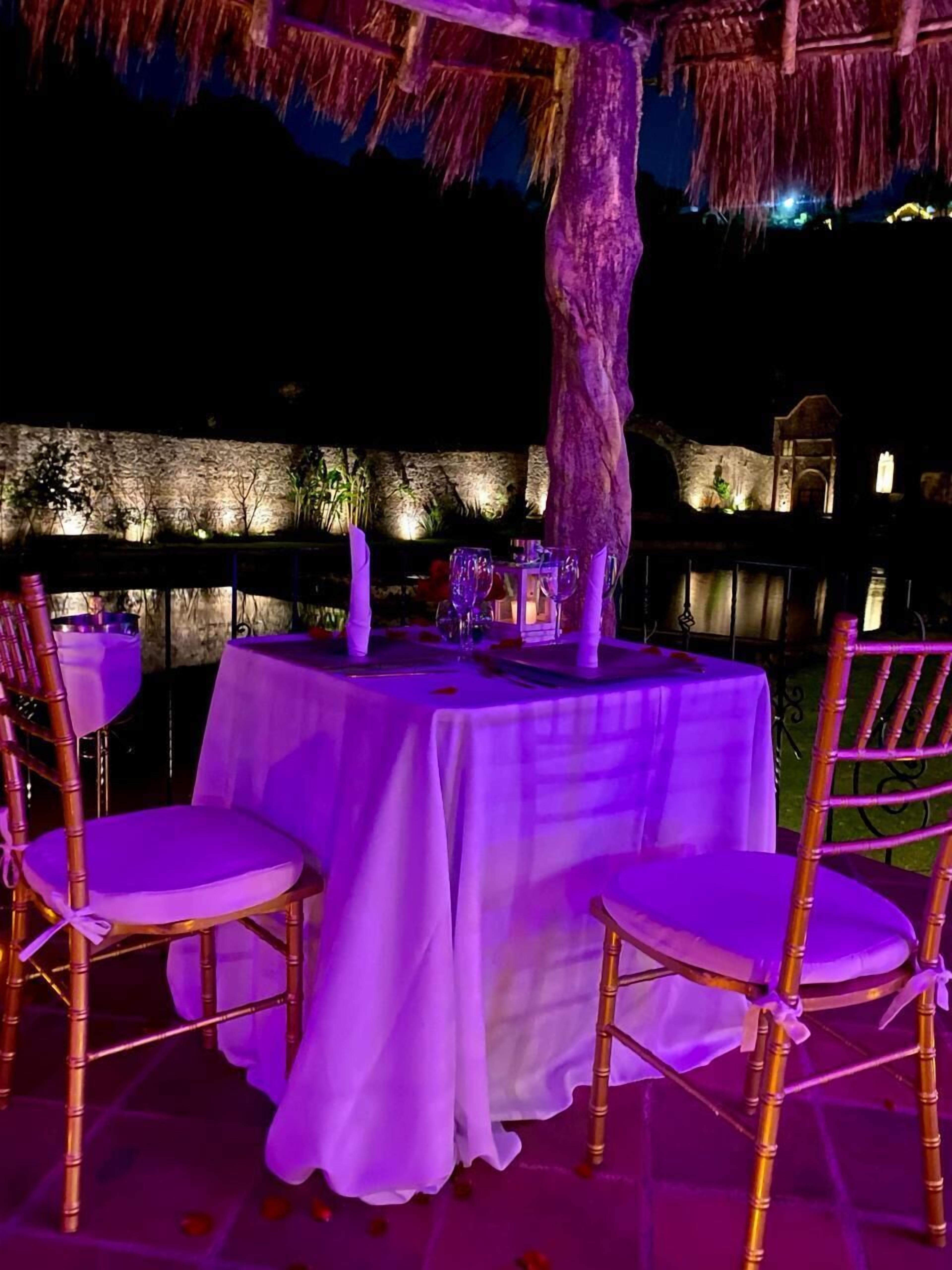 An outdoor dining area with round tables, chairs, and a thatched roof.