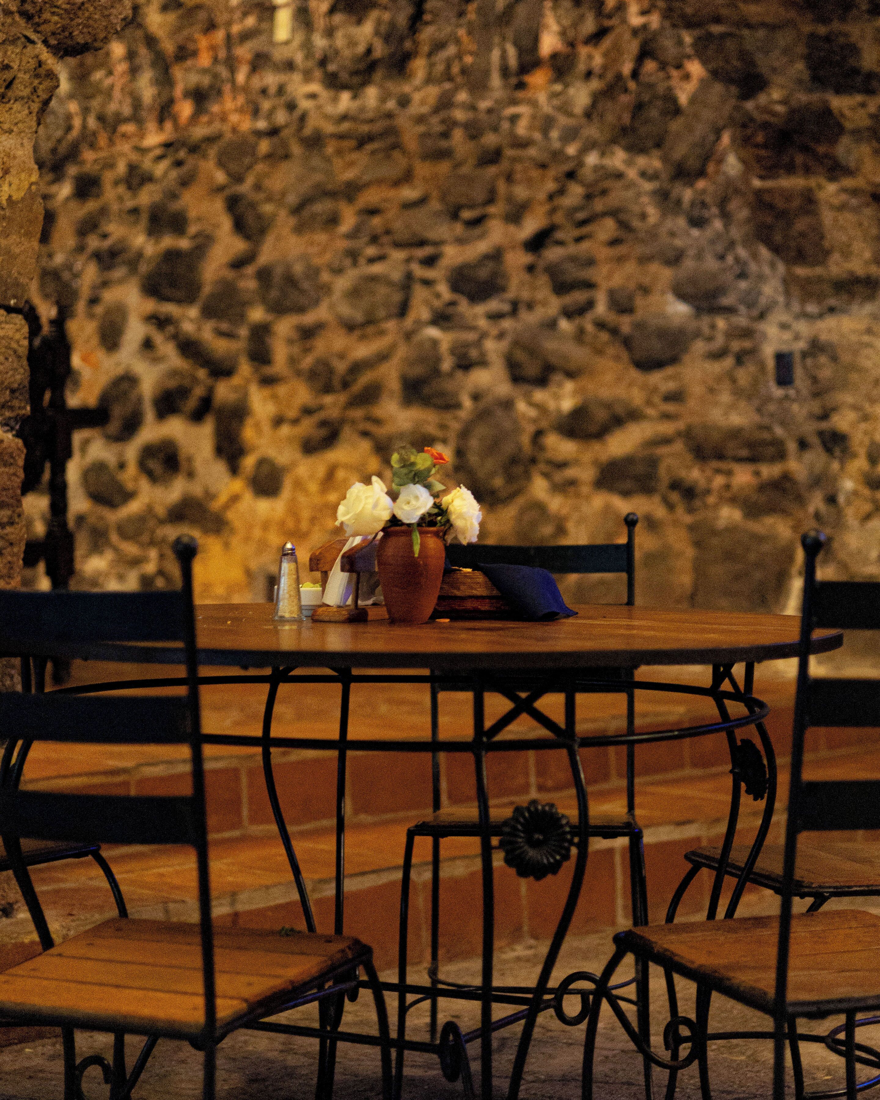 A stone wall, a wooden table with chairs, and a vase with flowers.