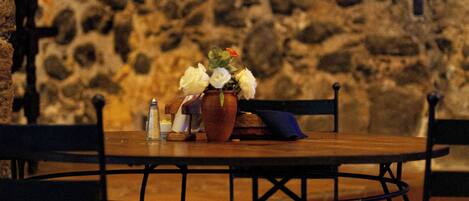 A stone wall, a wooden table with chairs, and a vase with flowers.