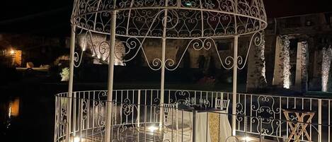 A gazebo with intricate metalwork, a table set for dining, and a railing surrounding the area.